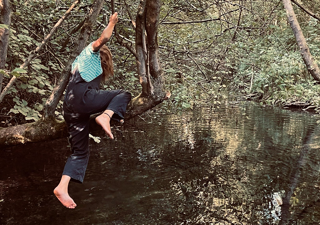 Frau klettert auf Baum am Wasser