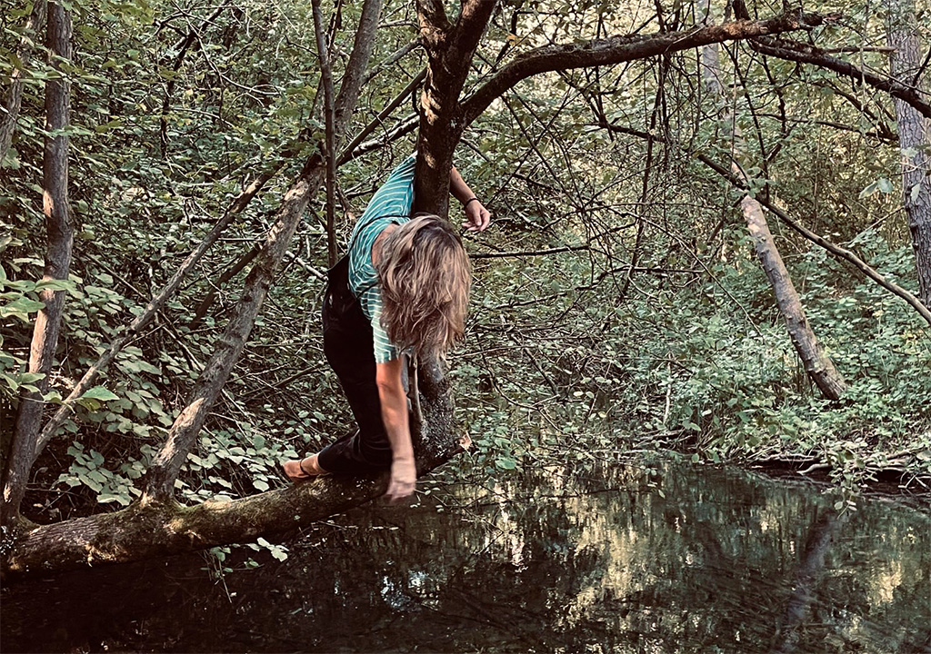 Frau klettert auf Baum am Wasser